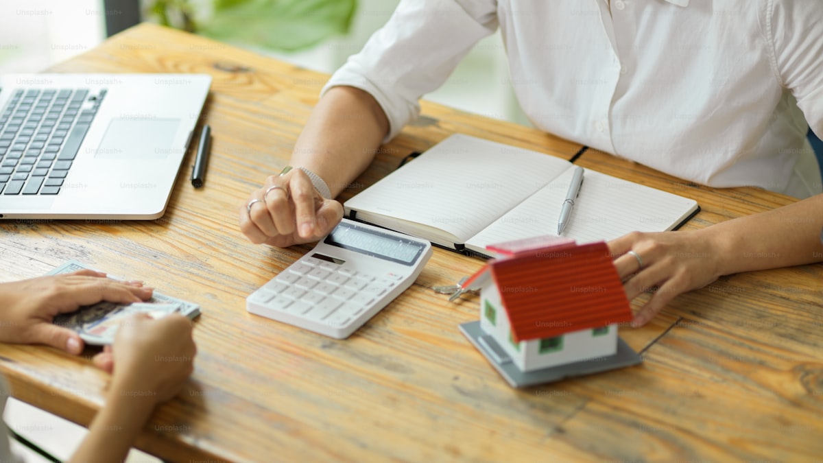 Real estate professional using calculator with house model and financial documents